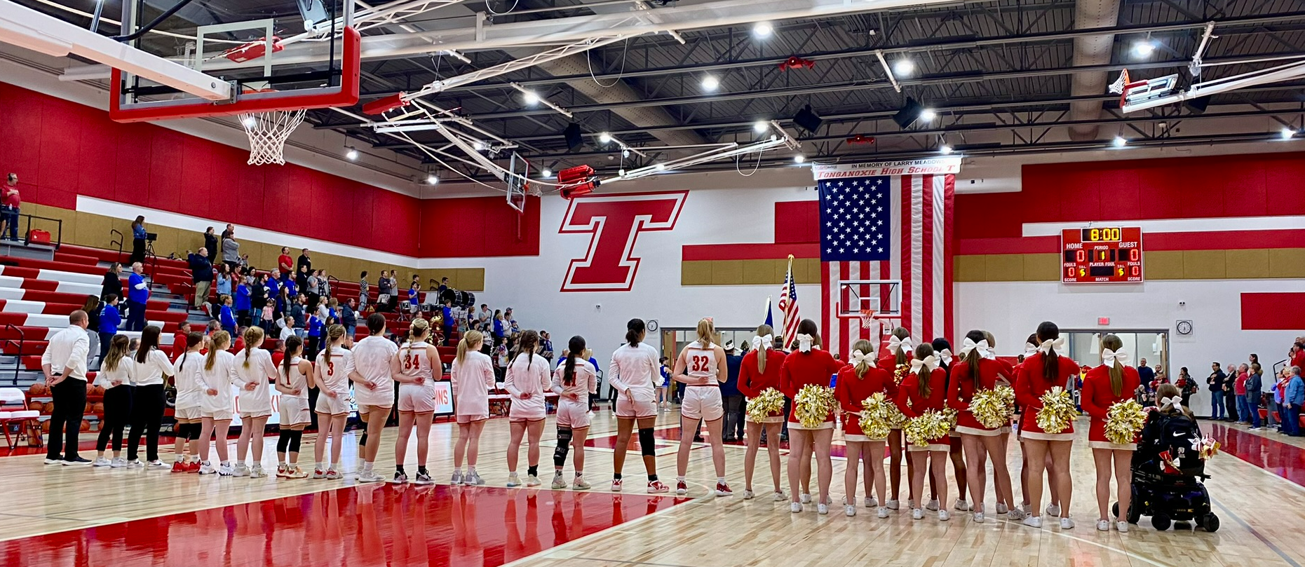 Girls basketball team and cheerleaders stand in a line on the basketball court while national anthem is played
