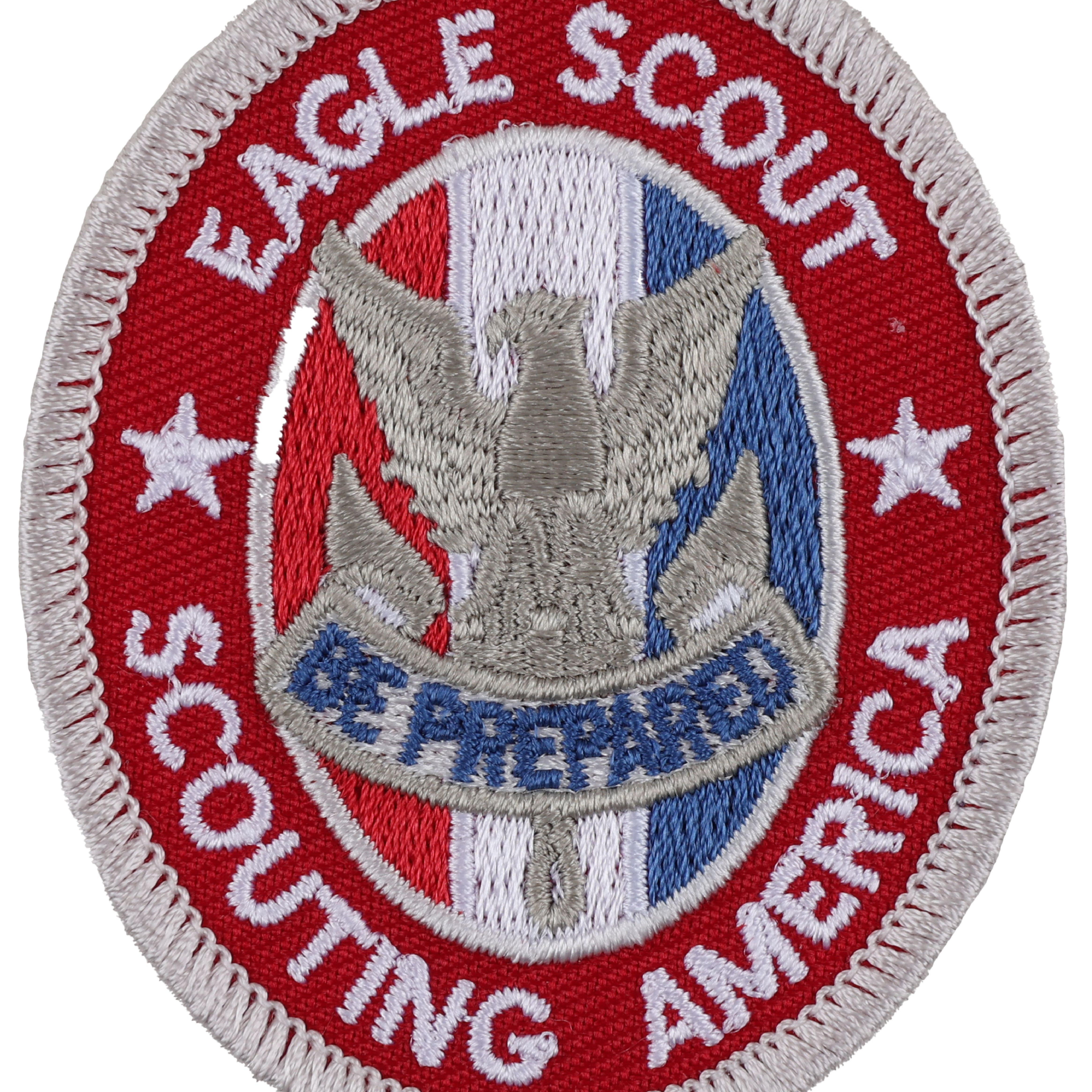 Round emblem with white border. Centered is an eagle with shield and olive branch. Text reads "EAGLE SCOUT" and "BE PREPARED" with stars and stripes on each side.