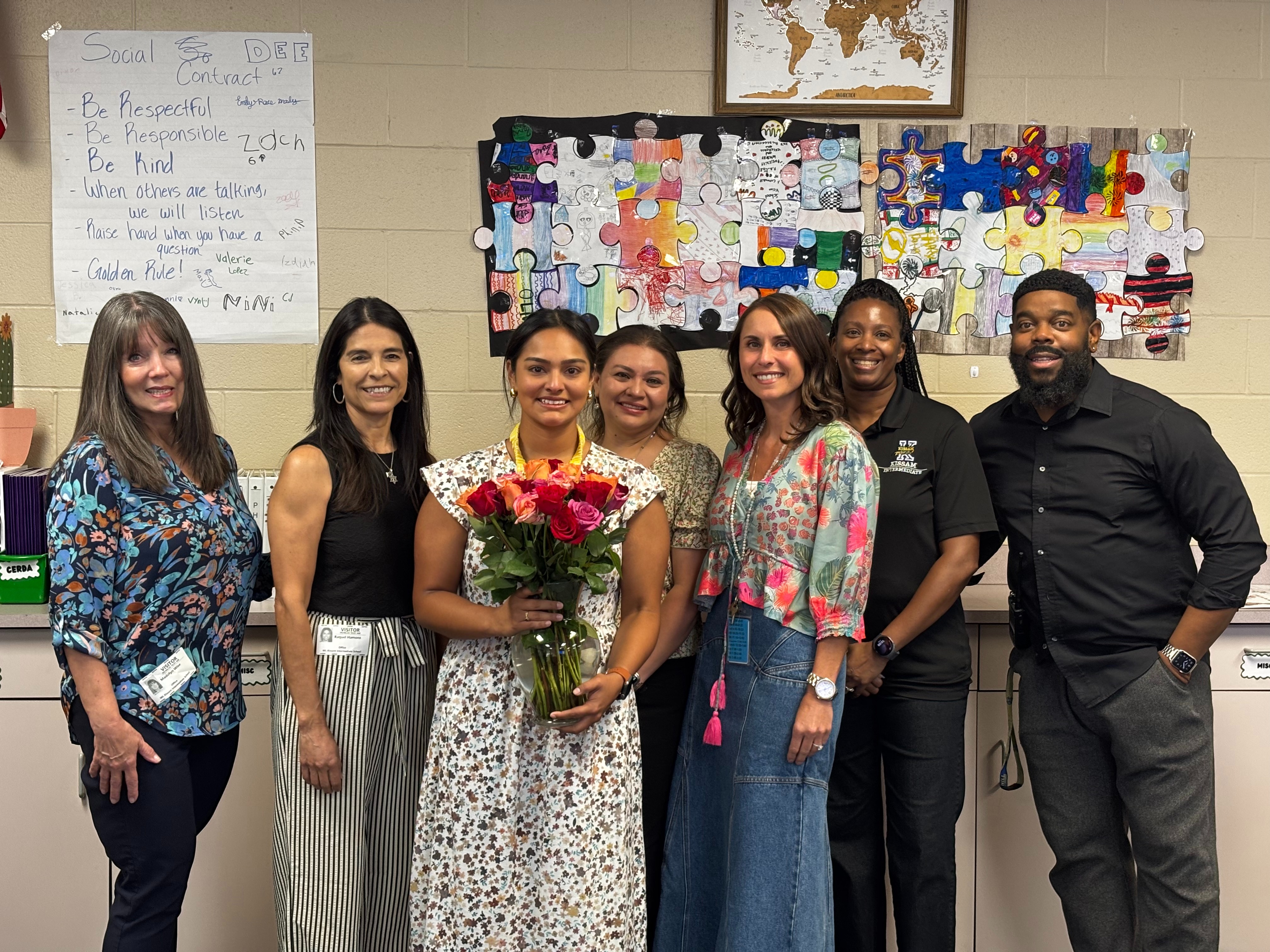 a group of Kissam staff stand with a teacher holding flowers who was awarded a grant