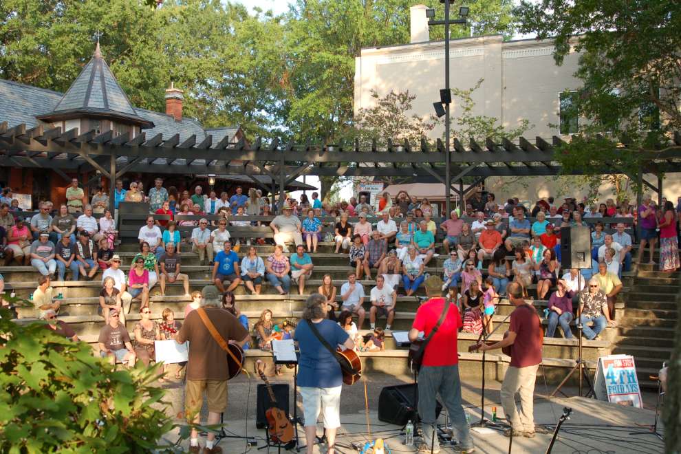 A crowd enjoying music of four acoustic guitar musicians at downtown Burlington park during the daytime