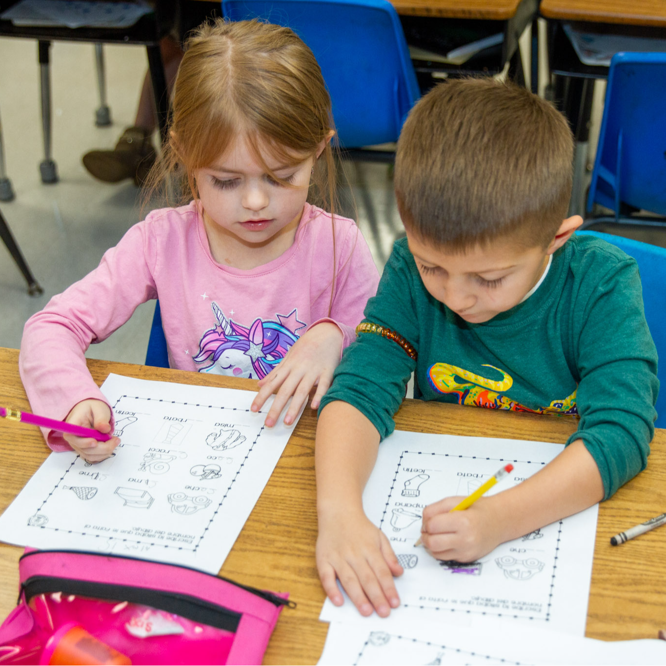Two kindergarten students work on a paper activity at their desks