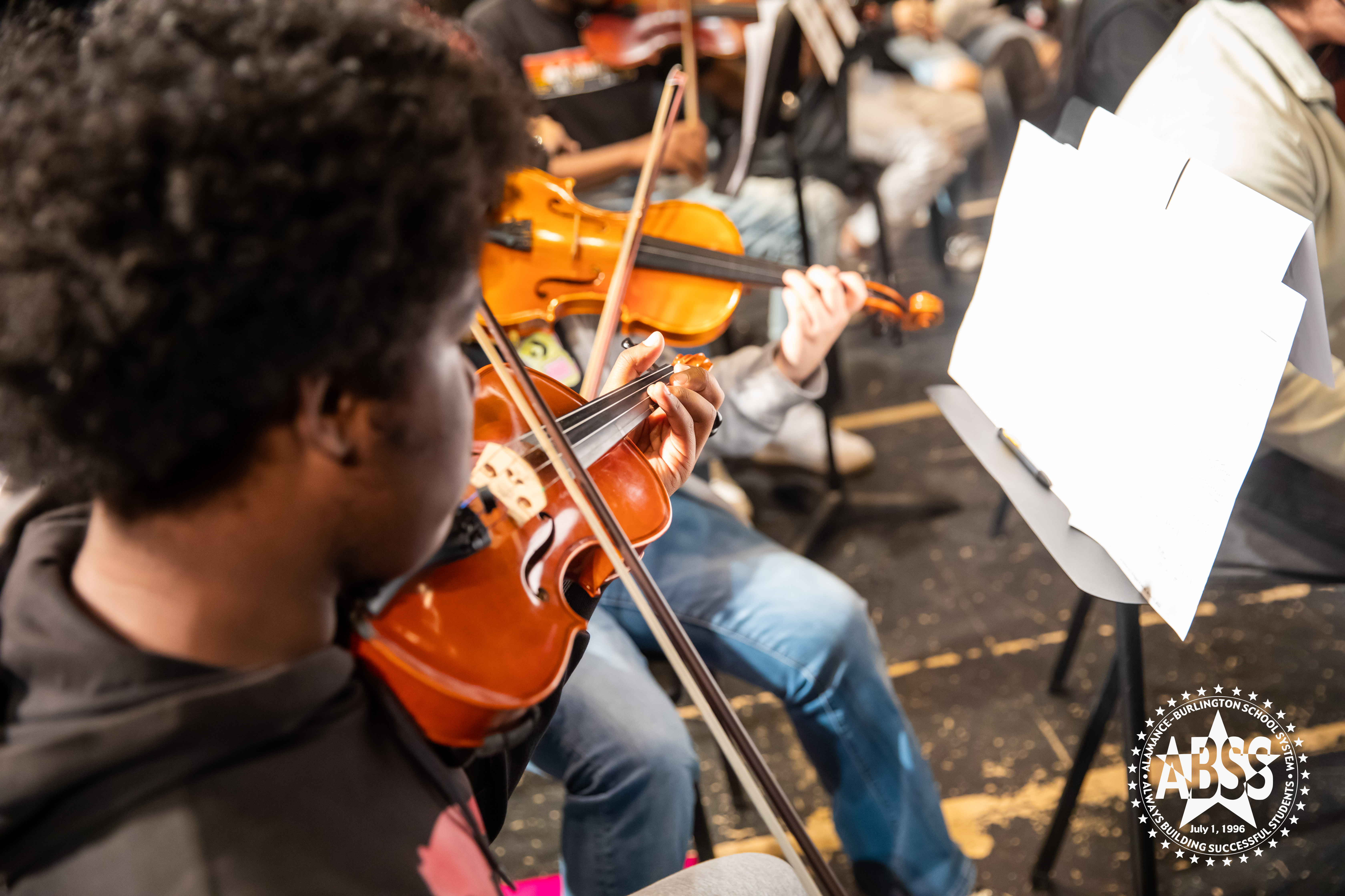 All-County Orchestra high school student looks at sheet music as he plays his violin