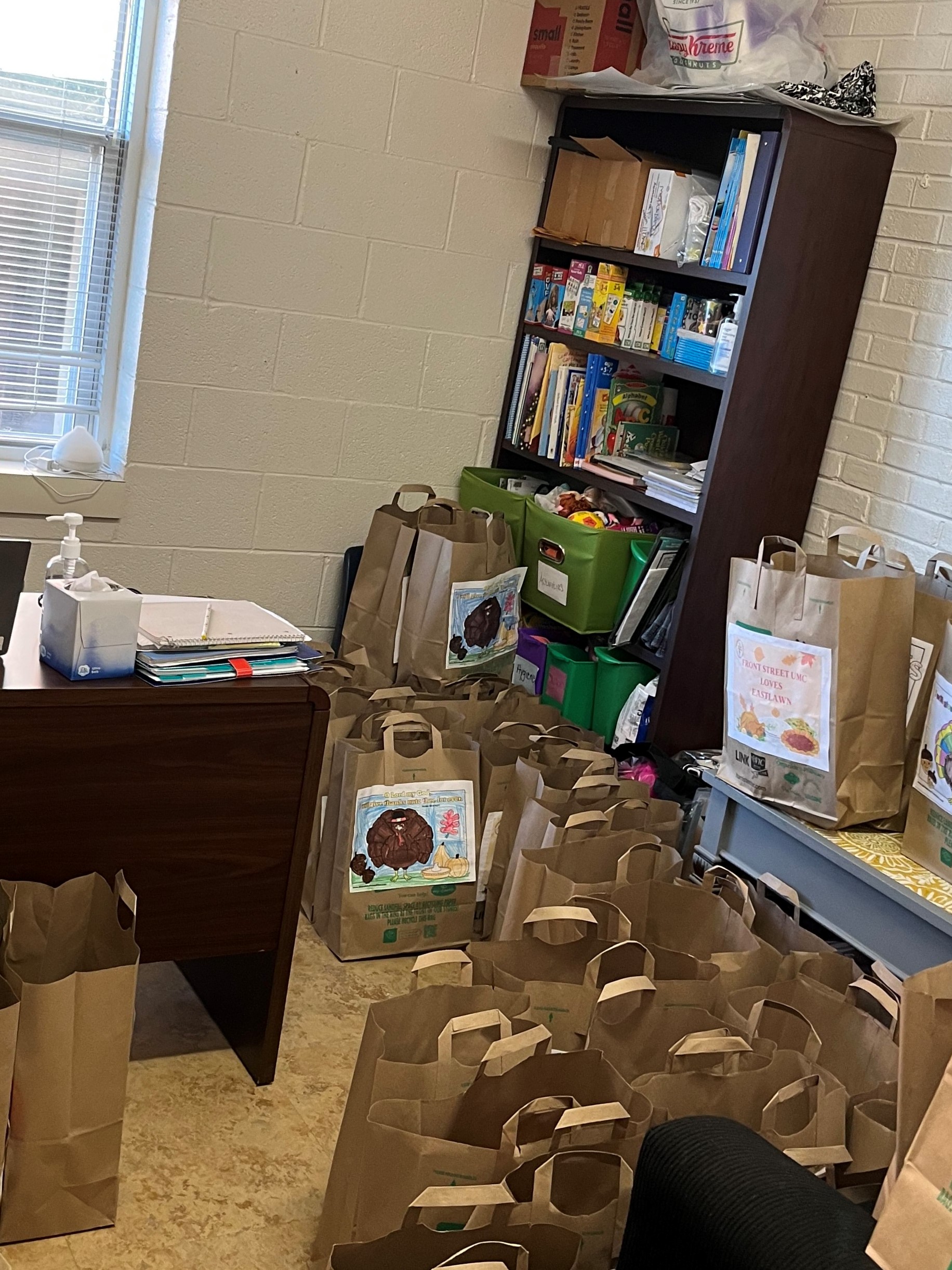 Sample of Thanksgiving Meals for families in need showing many large brown paper bags on the floor in an office filled with supplies