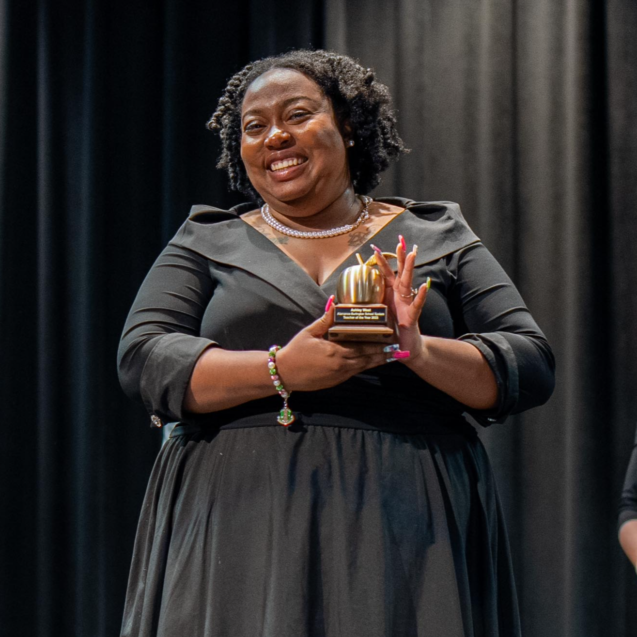 Teacher of the Year, Ashley West, on stage holding a golden apple trophy