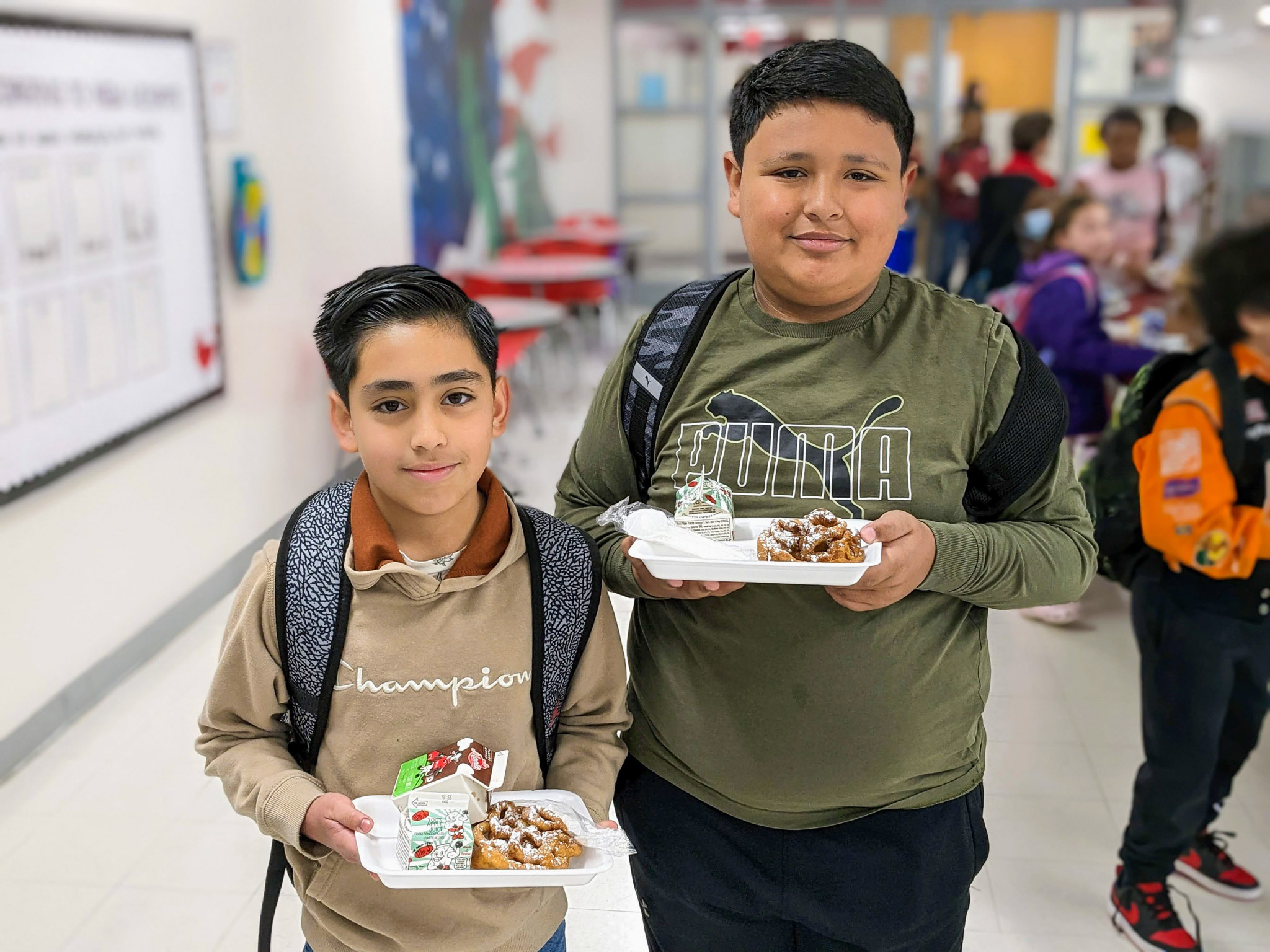 Two elementary students holding trays of food in the cafeteria
