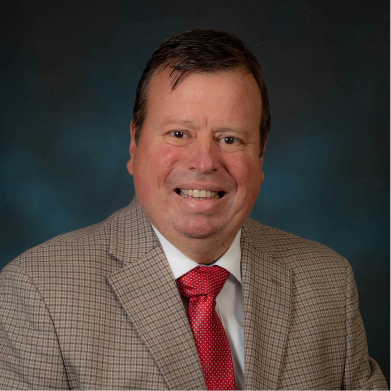 Dr. Matthew Haley wearing a brown plaid suit jacket, white shirt, and red tie