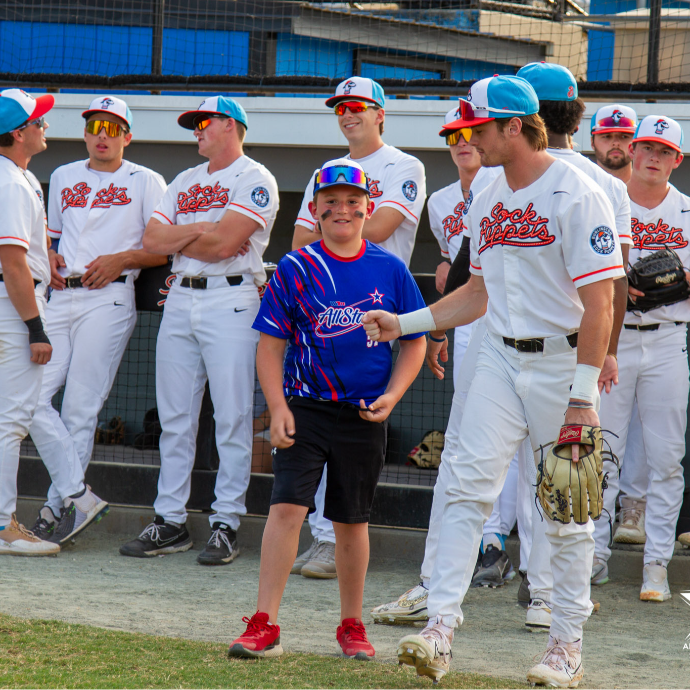 A player from the Sock Puppets baseball team holds out his fist for a first bump towards a student in a blue All Stars jersey