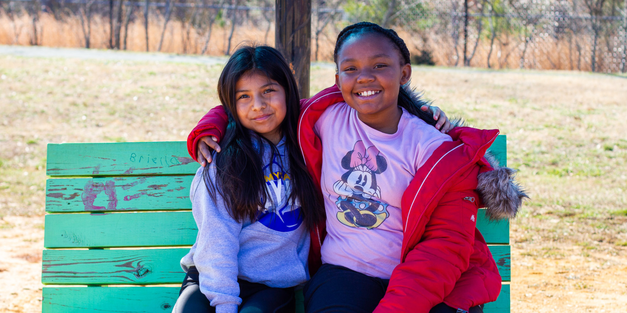 To girls sit on a green bench outside at Highland Elementary