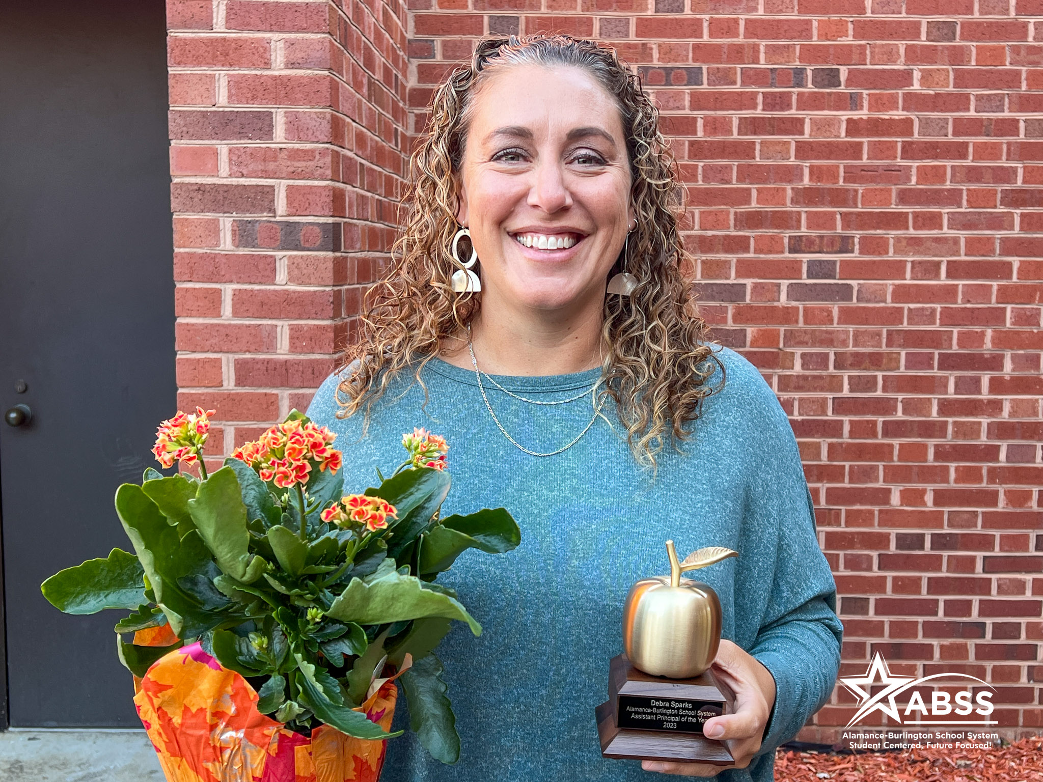 Debra Sparks holding flowers and a golden apple award