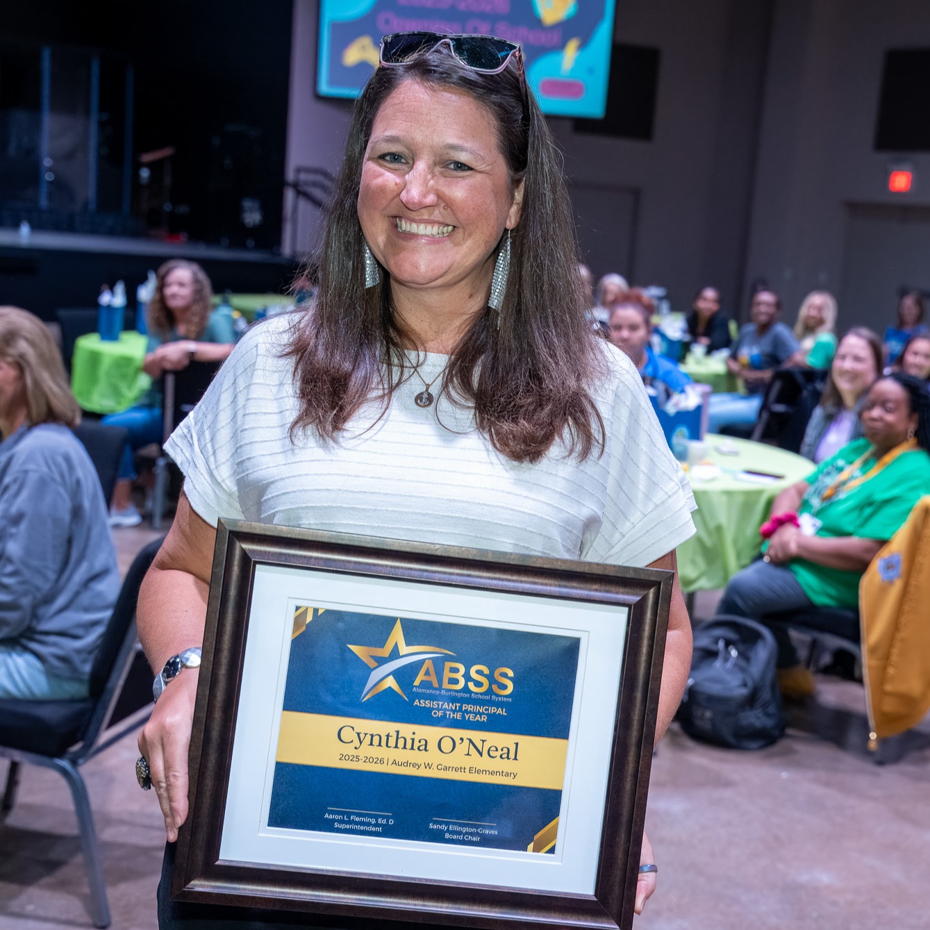 Cynthia O'Neal holding an Assistant Principal of the Year award in the middle of a group of staff at an opening staff meeting