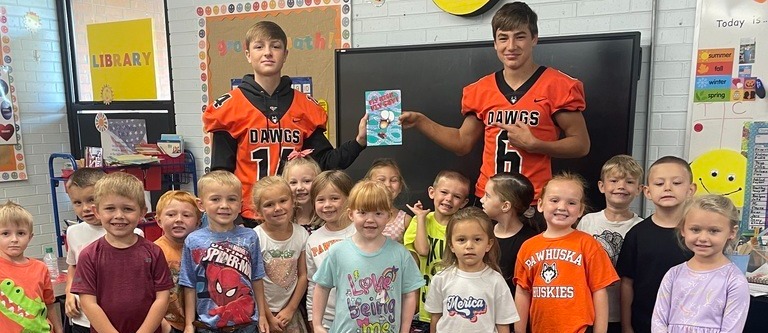 Two football players smile with elementary students