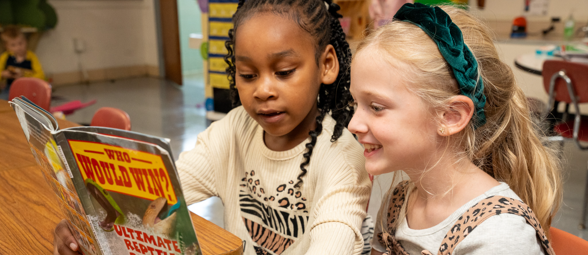 Two young girls sit side by side and look at a non-fiction book together