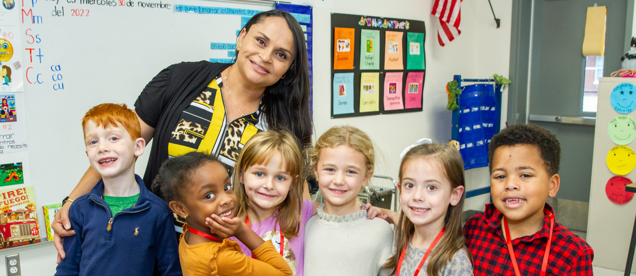Kindergarten teacher Aceneth Cruz standing behind six of her students on the carpet in her classroom at Elon Elementary