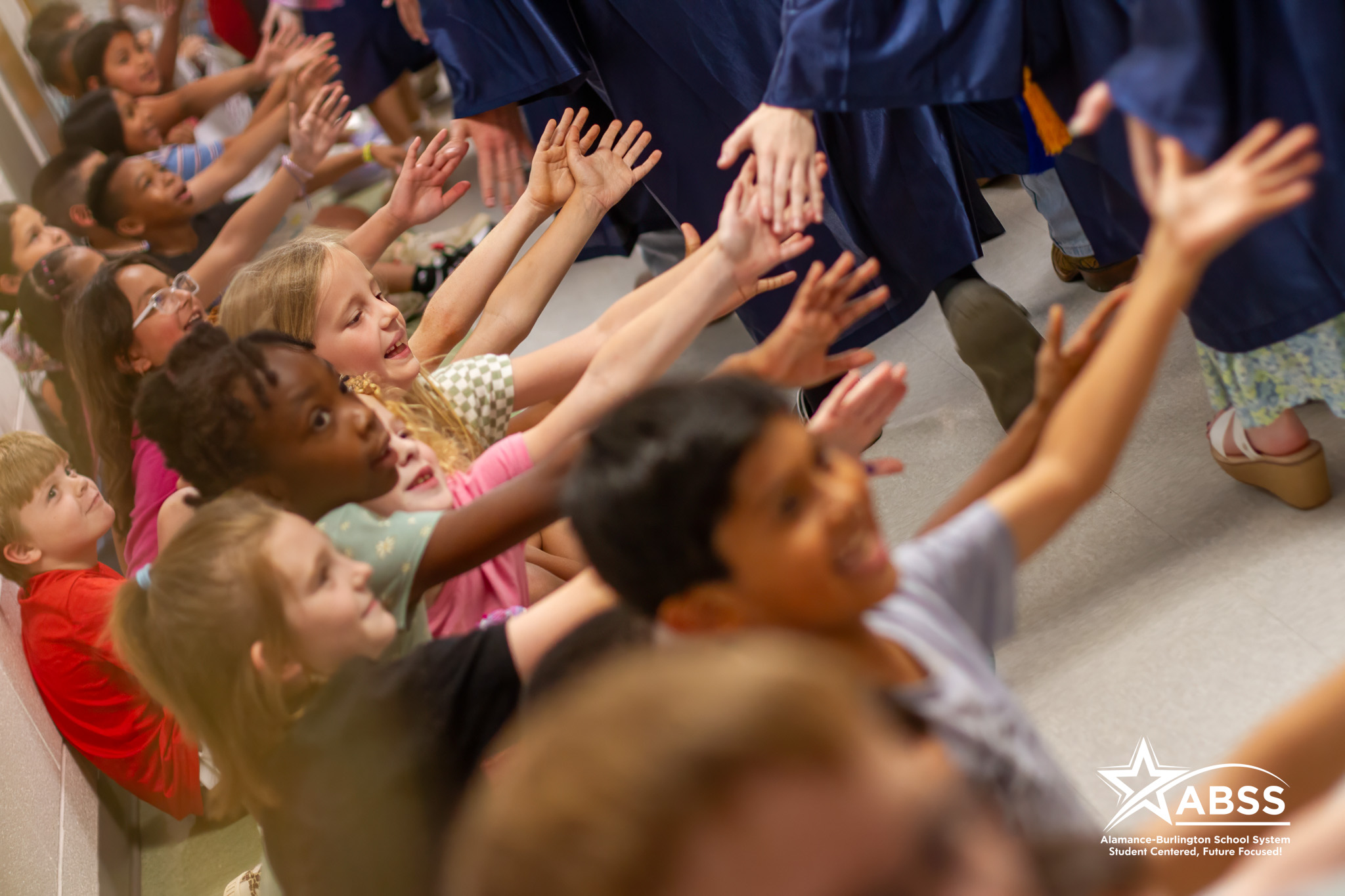Elementary students holding their hands out to high five senior graduates walking by