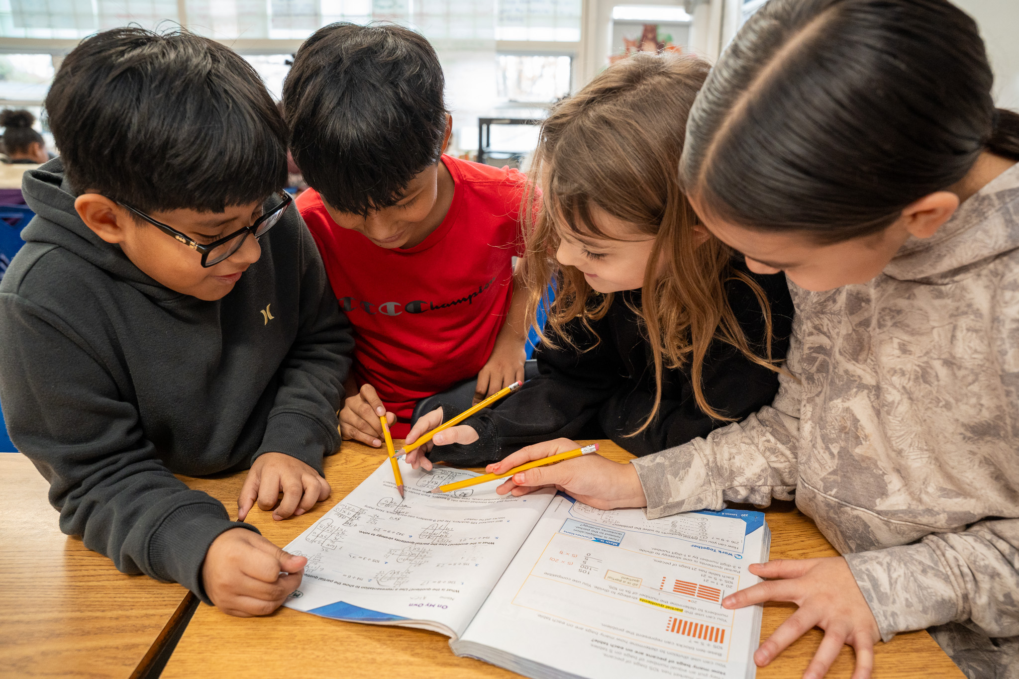 Four elementary students collaborate together on a math workbook problem