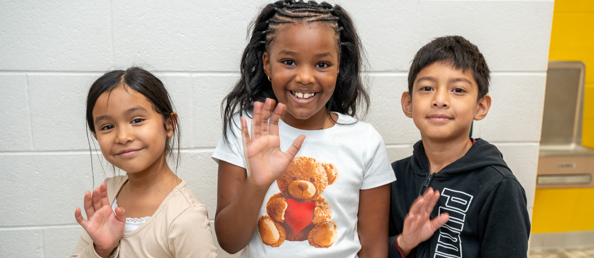 Three students smile enthusiastically in a school hallway