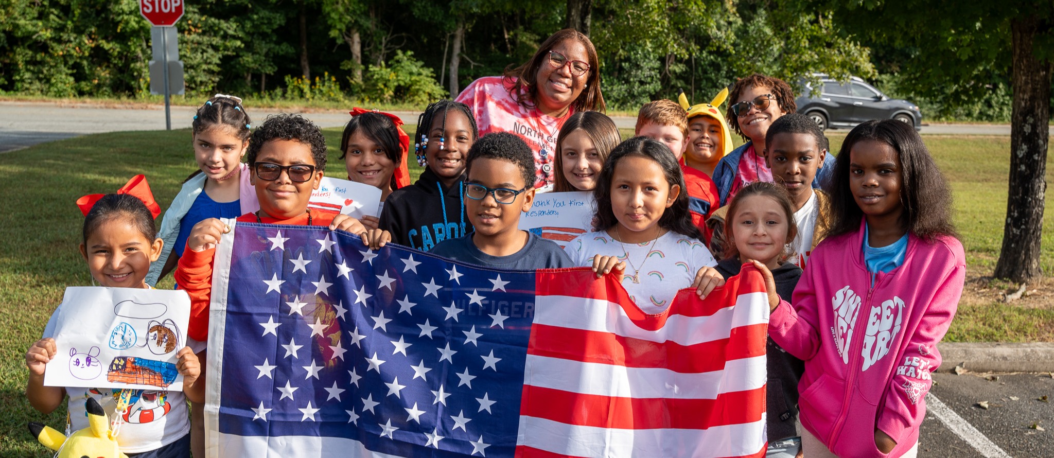 A group of elementary students stand with their teacher behind an American flag