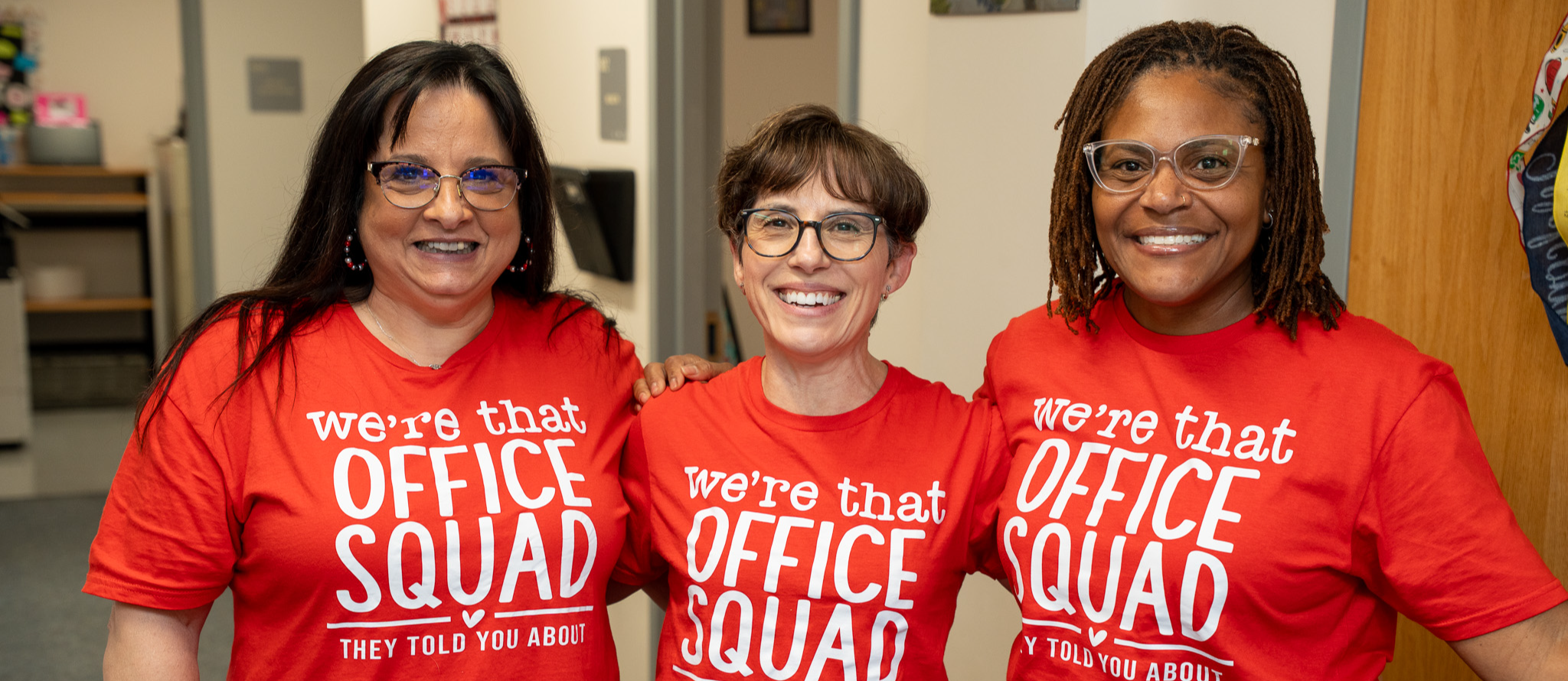 Three office staff in bright red shirts stand next to each other