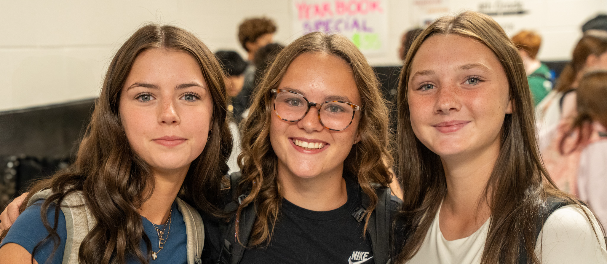 Three teenage girls standing beside one another during a class transition 