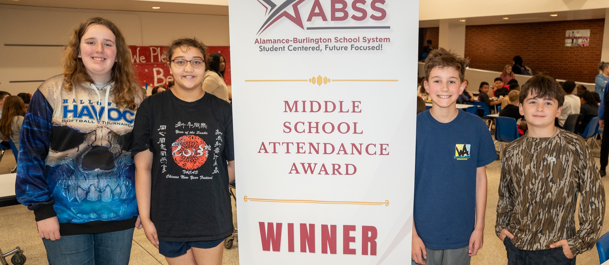 Four middle school students stand and smile around a Middle School Attendance Winner vertical banner