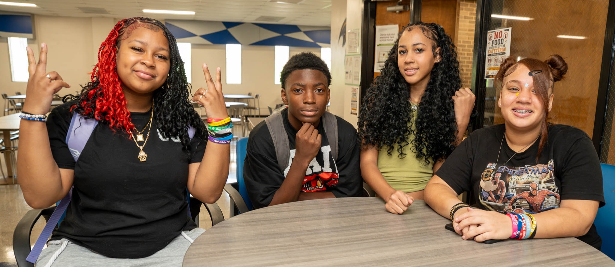 A small group of high school students around a circular table in a school cafeteria pose for a photo
