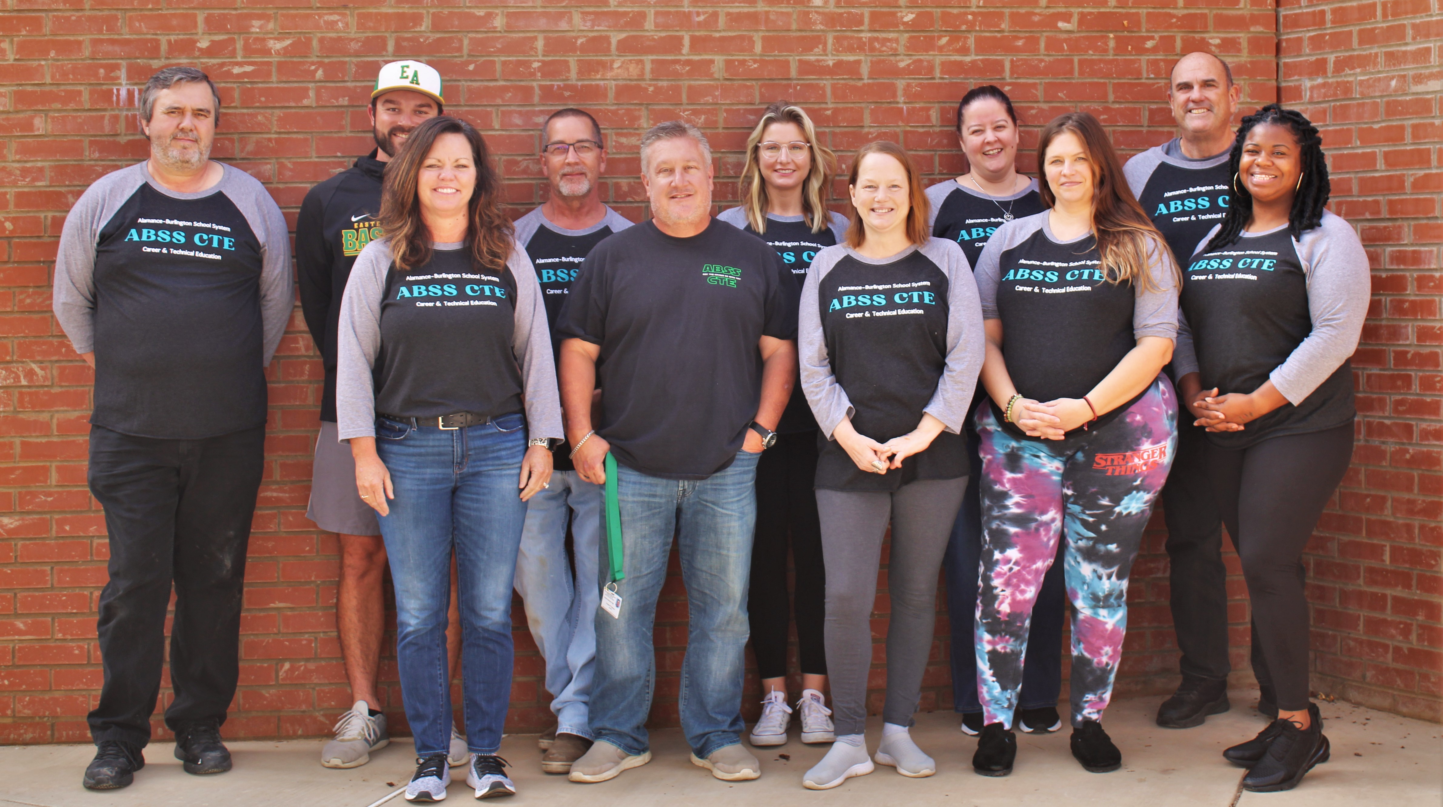 CTE Teachers standing together in two rows against a brick wall.