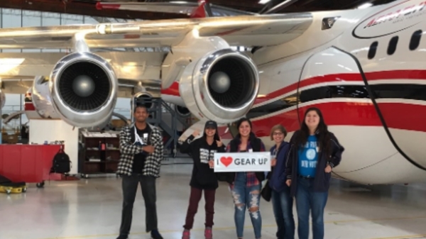 Students standing in front of a plane holding an I heart GEAR UP sign