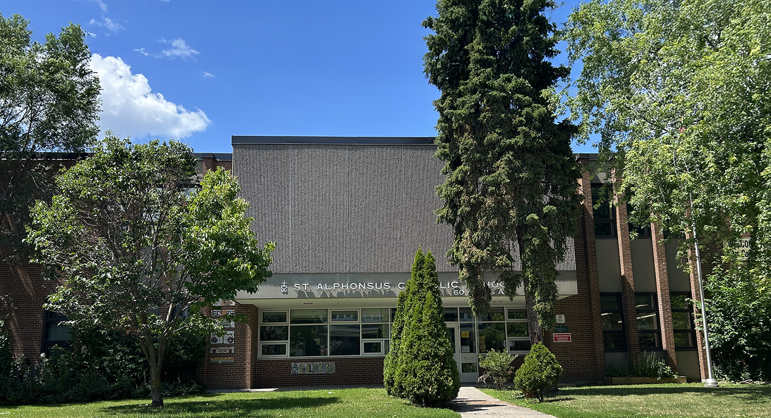 The front of the St. Alphonsus Catholic School building, showing a red brick building nestled between tall trees