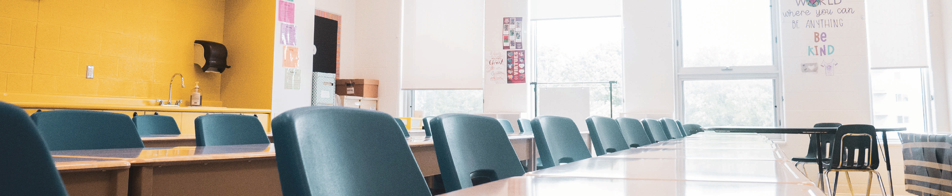 An image of an empty classroom with with yellow walls, windows and chairs. 