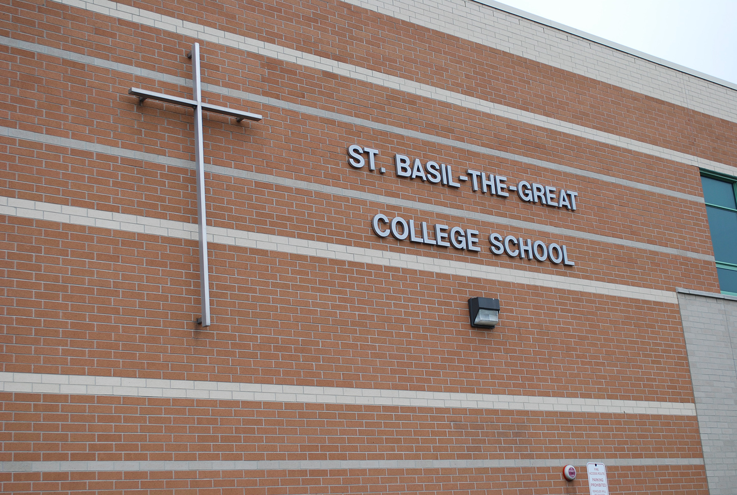 Photo of the St. Basil-the-Great College School building, showing a red brick building surrounded by trees and spacious school grounds