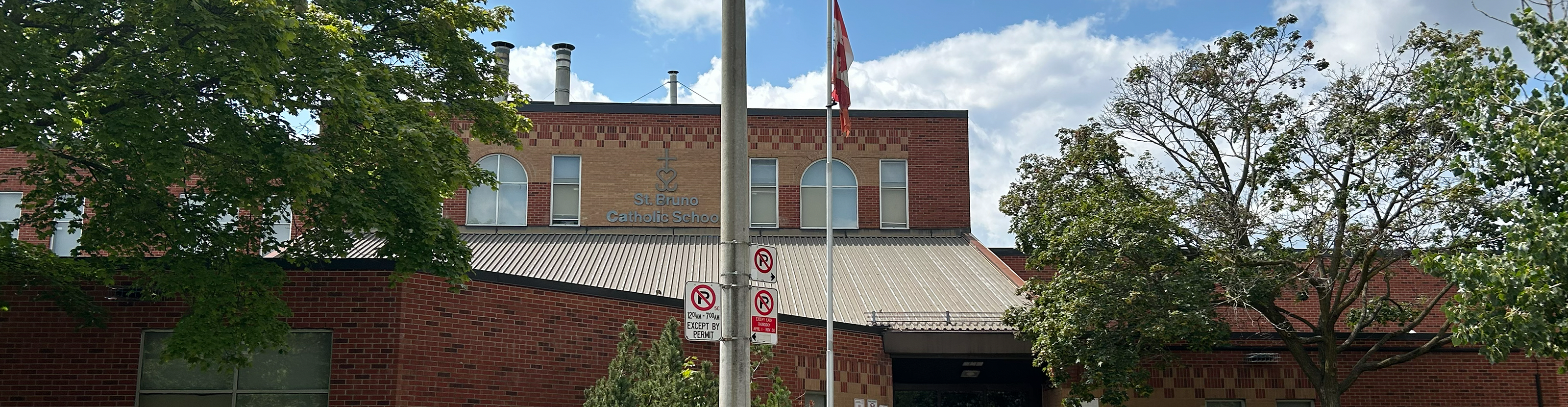 The front of the St. Bruno / St. Raymond Catholic School building, showing a red and orange brick building bordered by trees and greenery