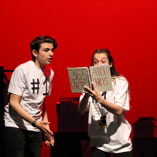 2 students reading a book on stage.