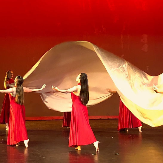 A group of students dancing on stage in red costumes. 