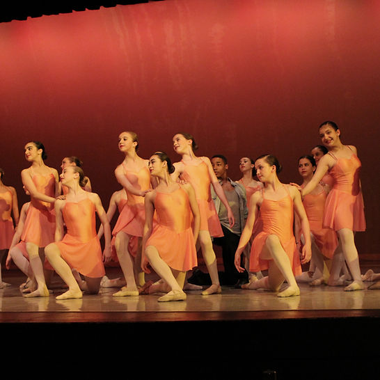 A group of students dancing on stage in pink dresses. 