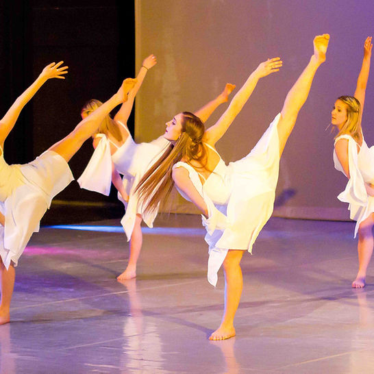 A group of students dancing on stage in white dresses. 