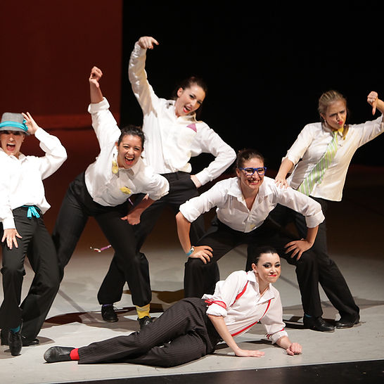 A group of students dancing on stage in black and white costumes. 