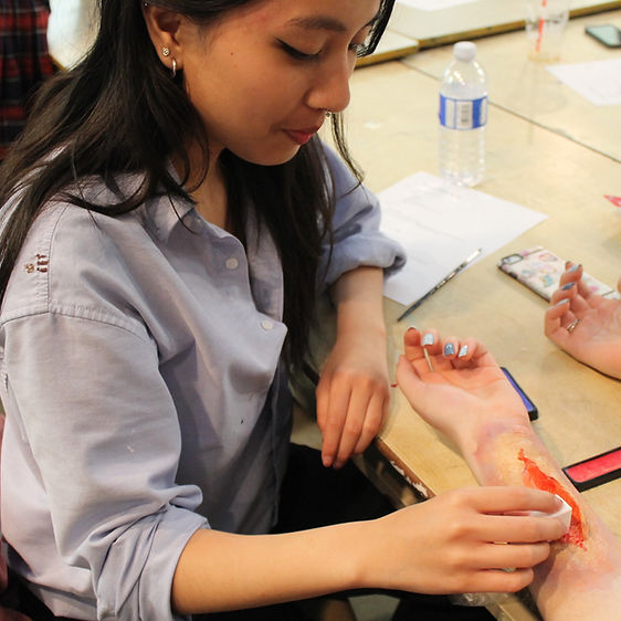 A student putting make up on another student's arm.