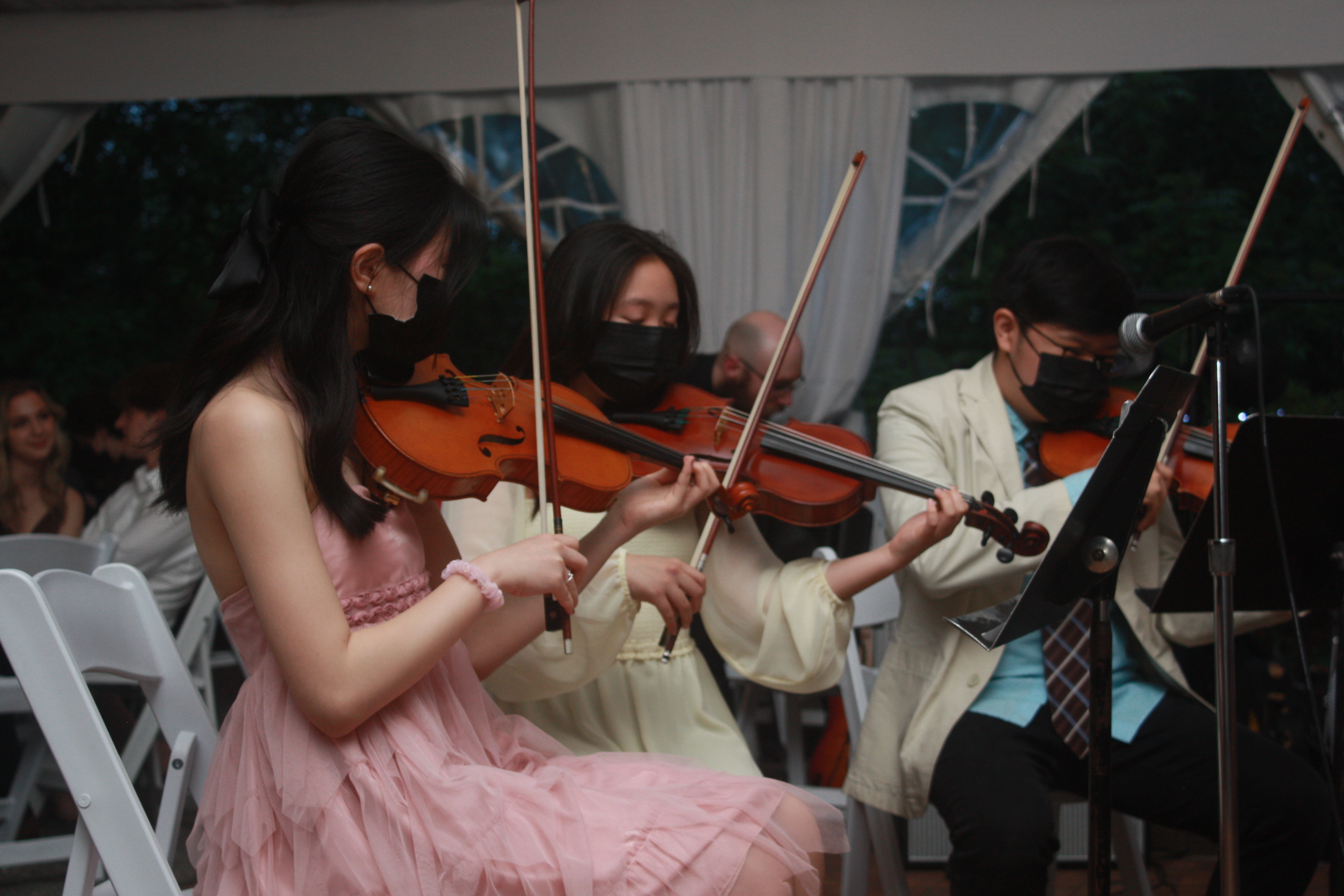 3 students playing violin at an event.