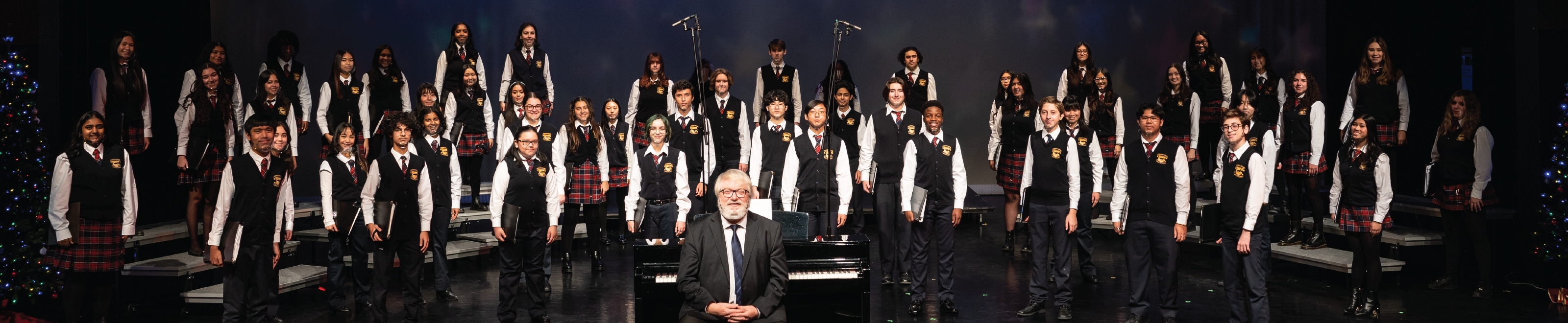 A group of vocal students standing on stage along with an instructor. 