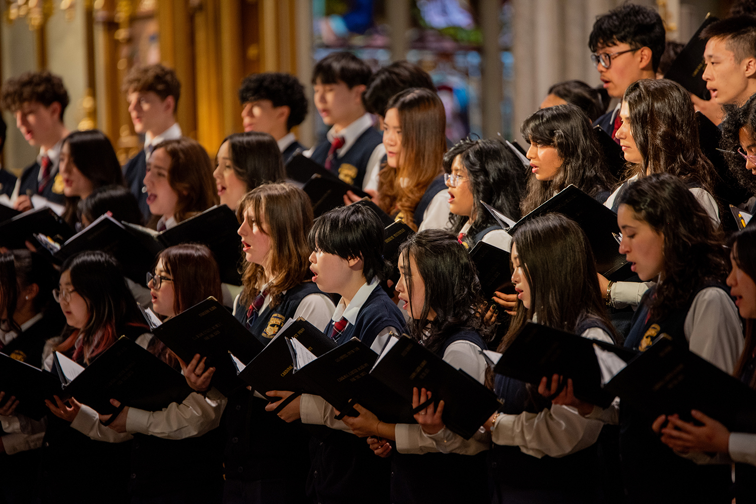 The Cardinal Carter sings from black folders in a warmly lit hall