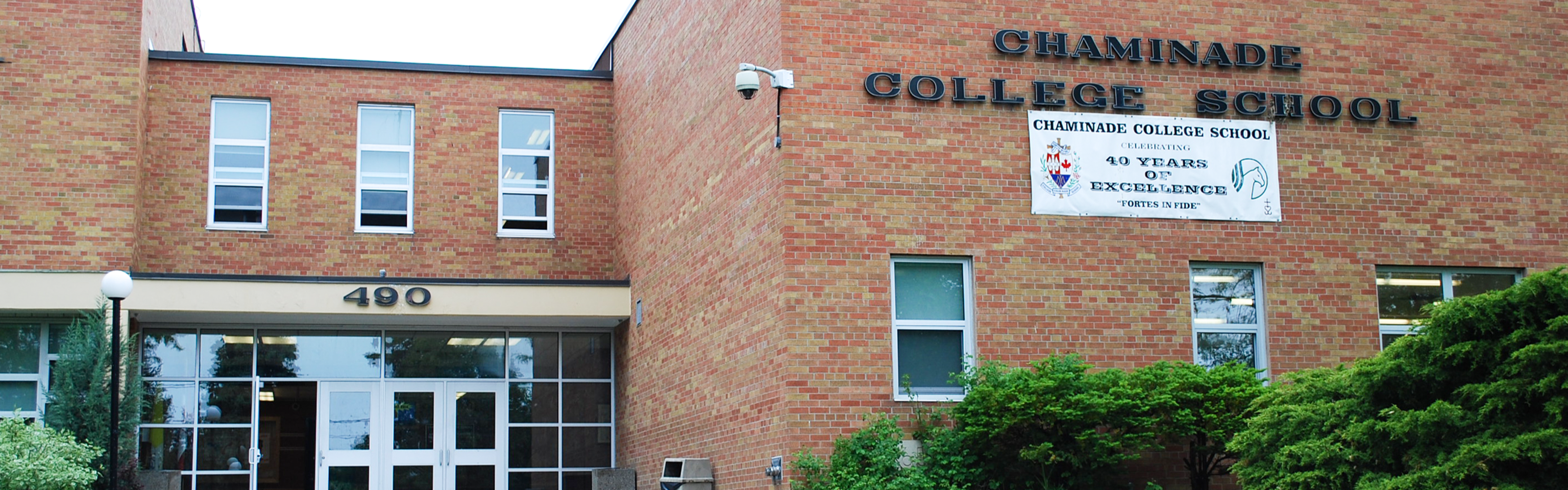 Photo of the Chaminade College School building, showing a red brick building with a windowed entrance, the school's name in black text, with a white banner under it recognizing the school's fourty year anniversary. 