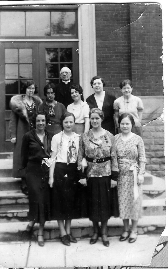 Old black and white staff photo of St. Cecilia, showing the staff standing together in front of the school.