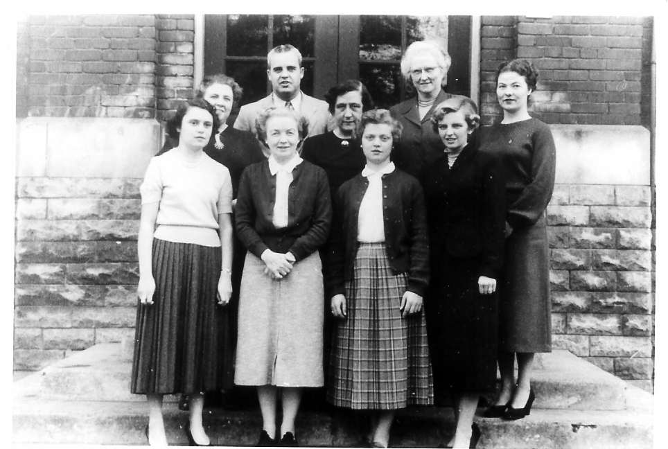 Old black and white staff photo of St. Cecilia, showing the staff standing together in front of the school.