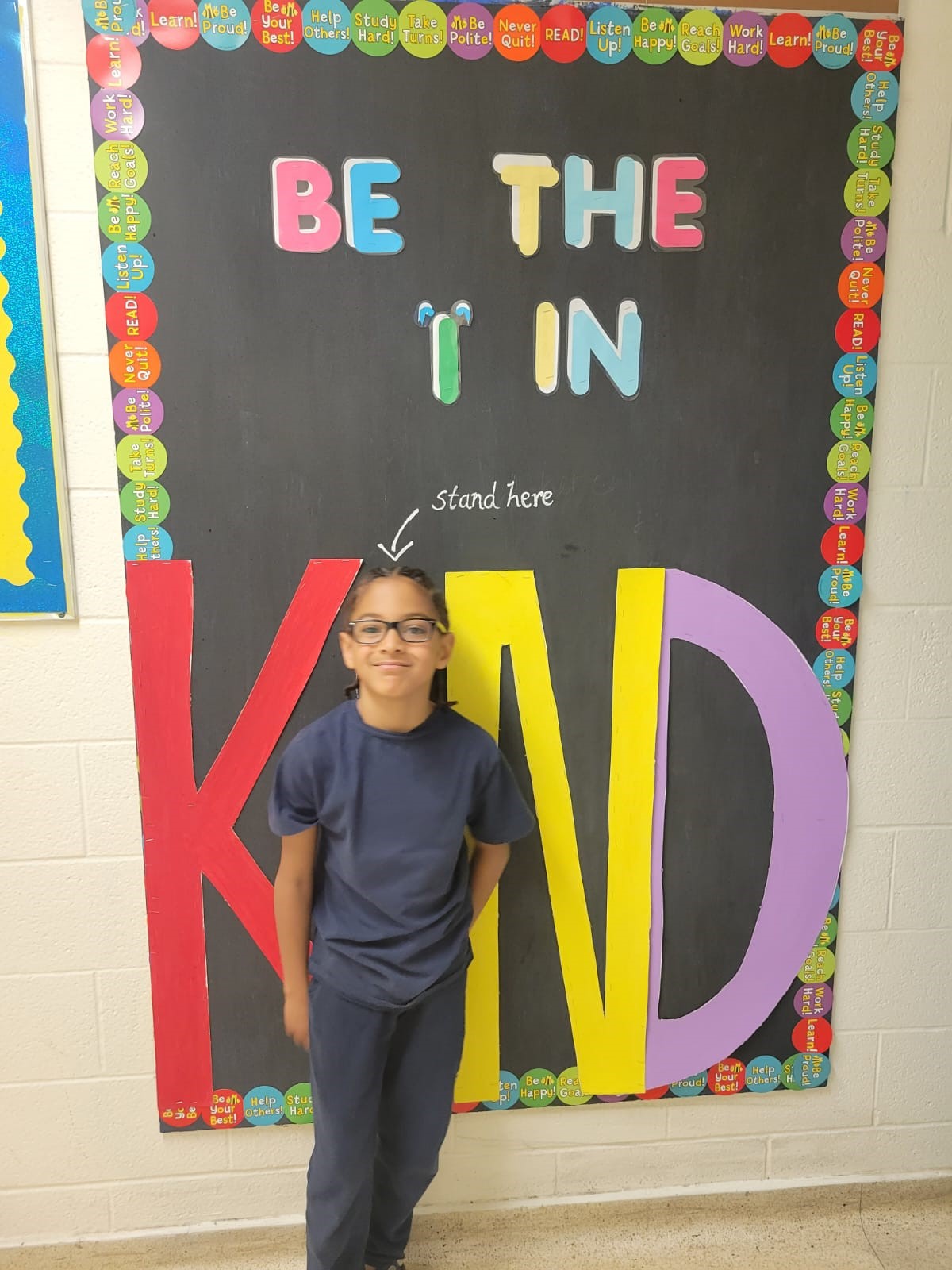 Student in uniform posing in front of a "Be the I in Kind" poster