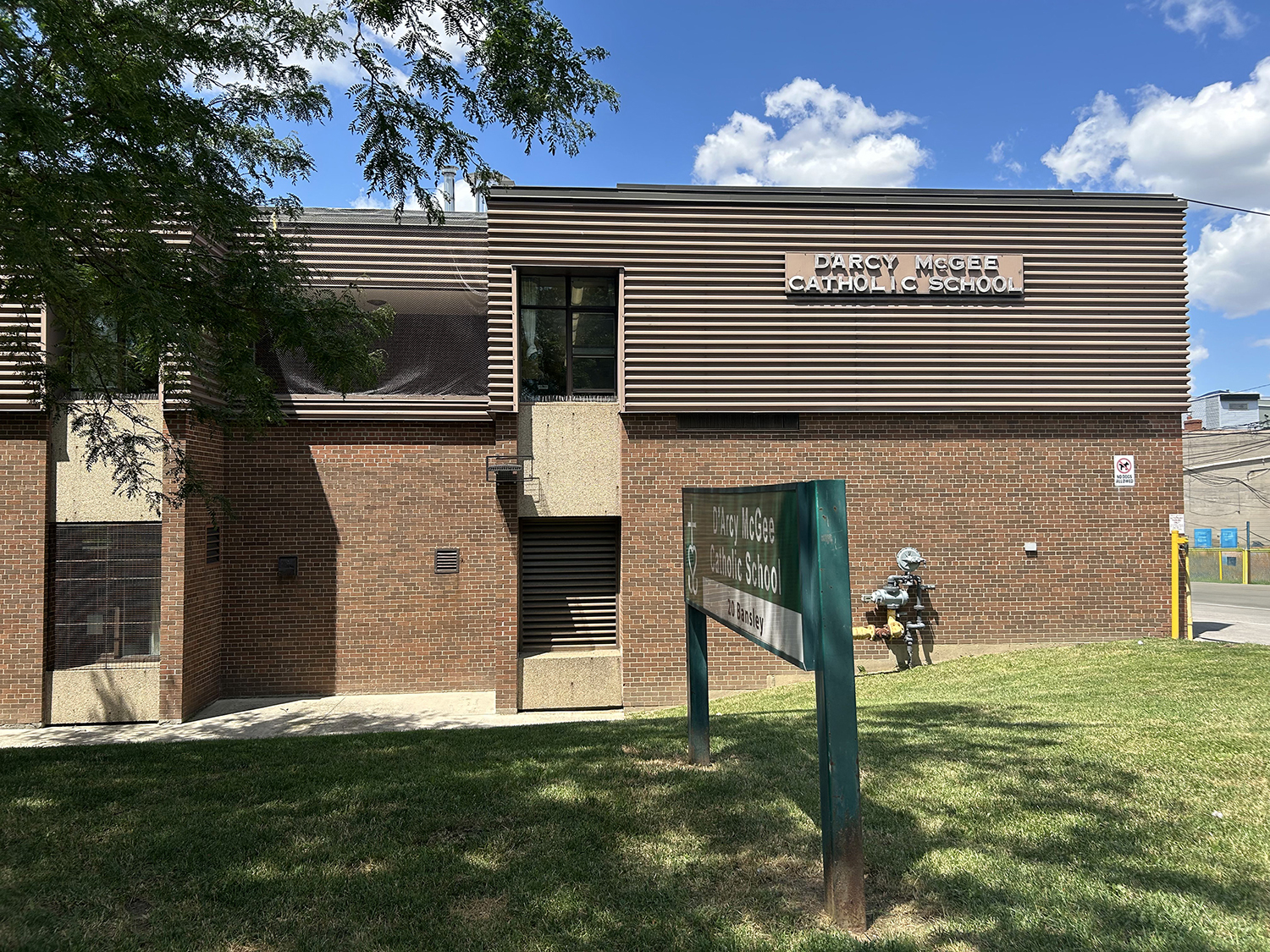 The front of the D'Arcy McGee Catholic School building, showing a sprawling red brick building bordered by large trees and greenery