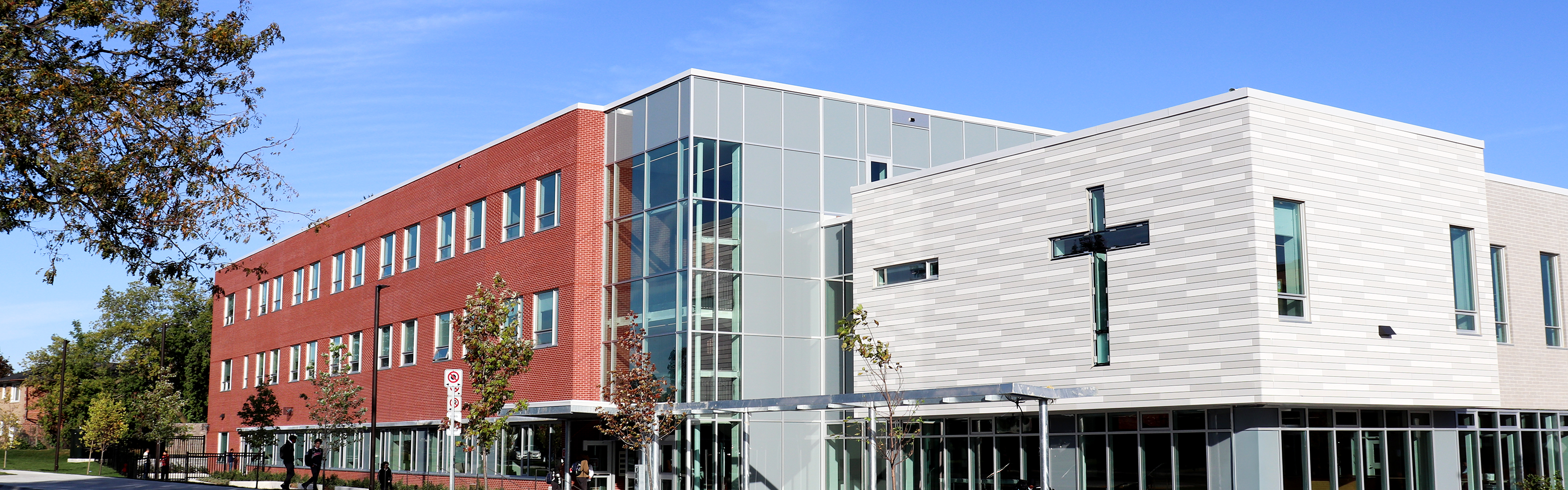 Photo of the Dante Alighieri Catholic Secondary School building, showing a red and grey brick building against a brilliantly blue sky