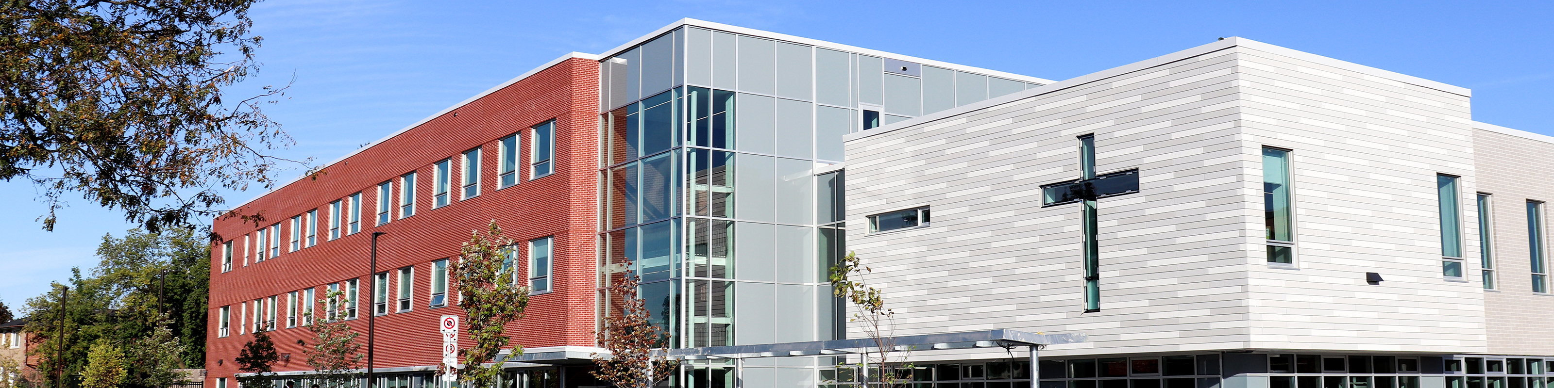 Photo of the Dante Alighieri Catholic Secondary School building, showing a red and grey brick building against a brilliantly blue sky