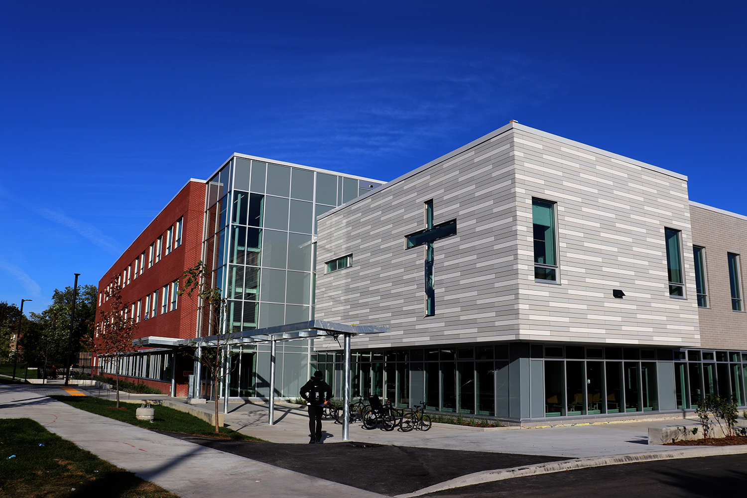 Photo of the Dante Alighieri Catholic Secondary School building, showing a student walking into a red and grey brick building against a brilliantly blue sky