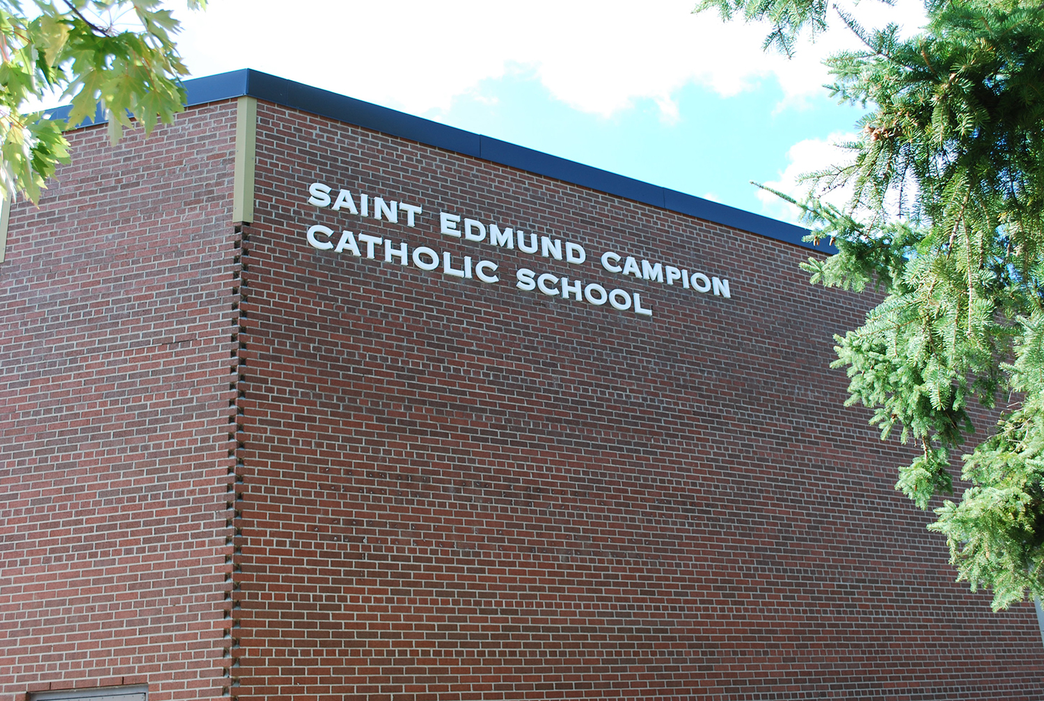 Photo of the St. Edmund Campion Catholic School, a red brick building surrounded by some trees