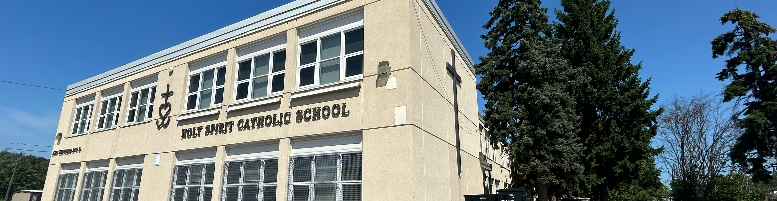 Photo of the Holy Spirit Catholic School building, a beige building looking out onto a busy road, with some trees around it and the school grounds
